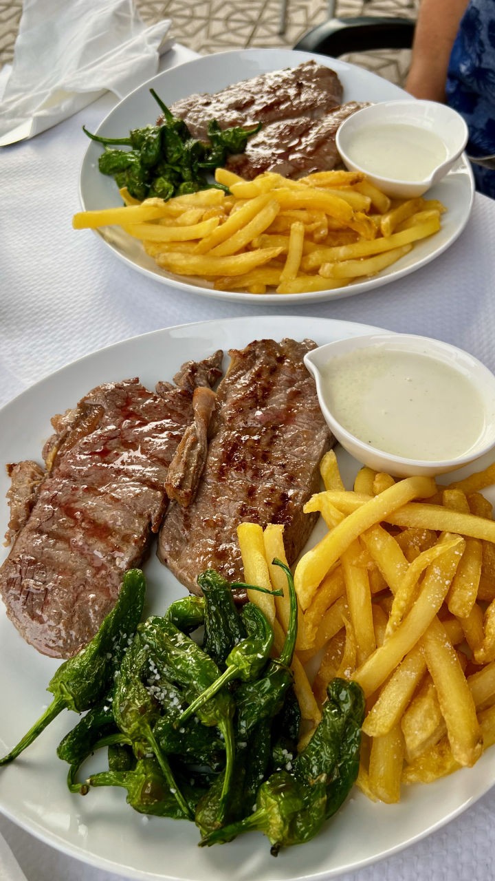Zwei Entrecotes mit Pommes, Pimientos und leckerer Käsesauce in einem Teller.